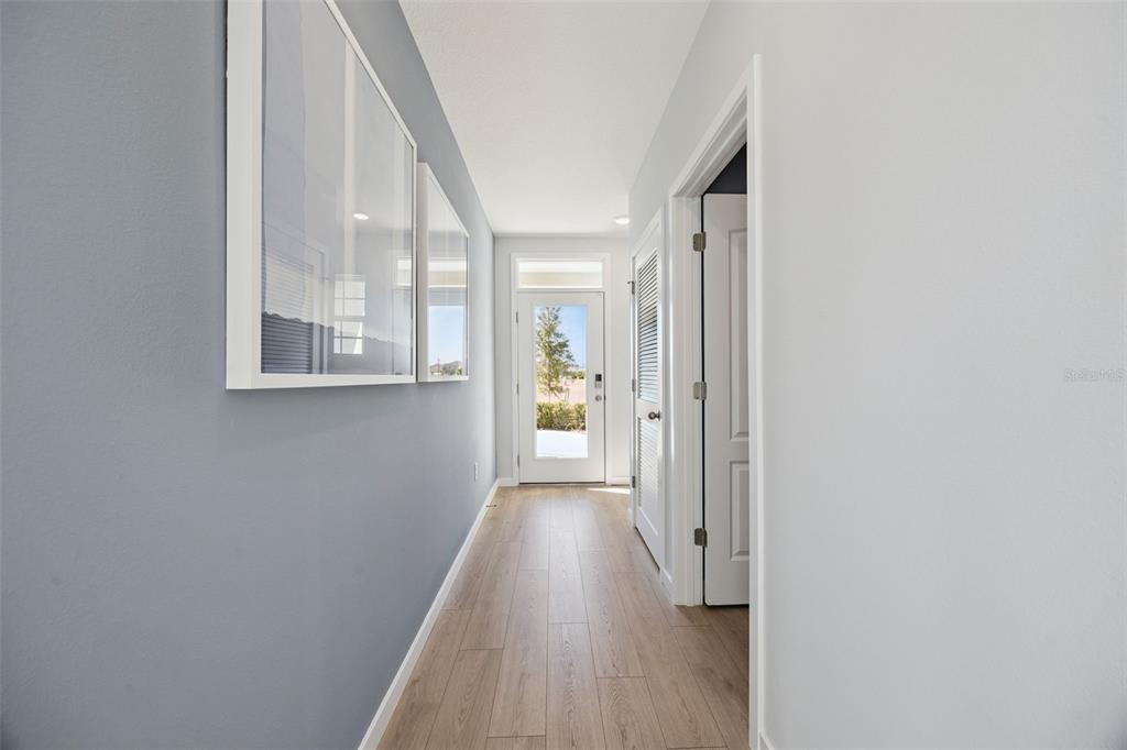 A hallway with light wood flooring, gray walls, framed art, and a glass-paneled front door — 1358 CAMELLIA BLOOM LANE, SANFORD, FL