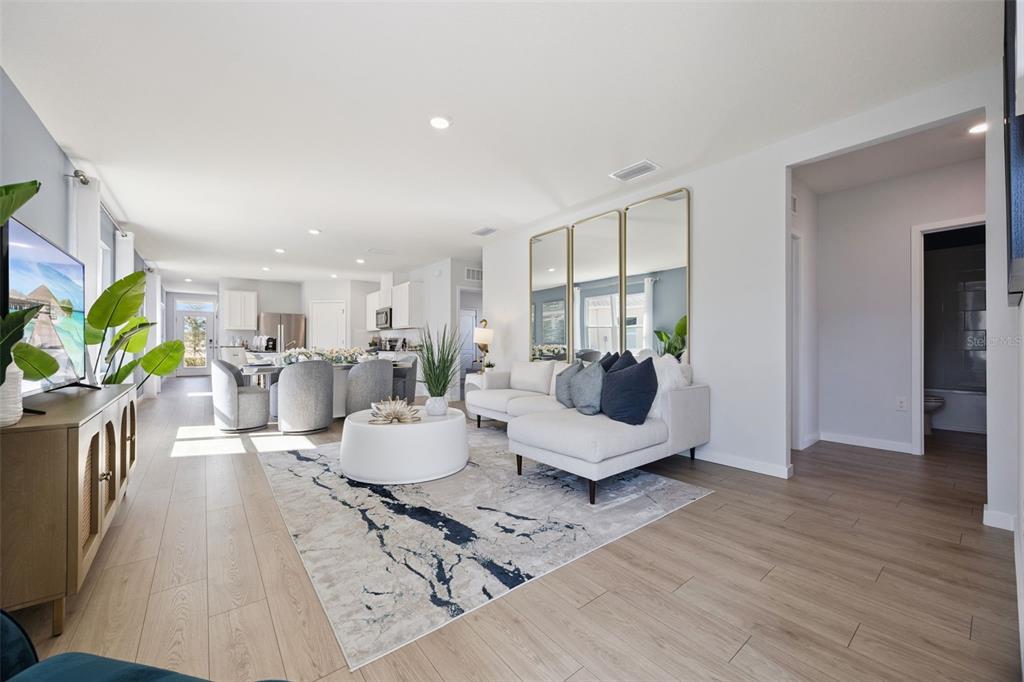 A bright, open-concept living room features light wood flooring, a white sectional, and gold-framed mirrors — 1358 CAMELLIA BLOOM LANE, SANFORD, FL