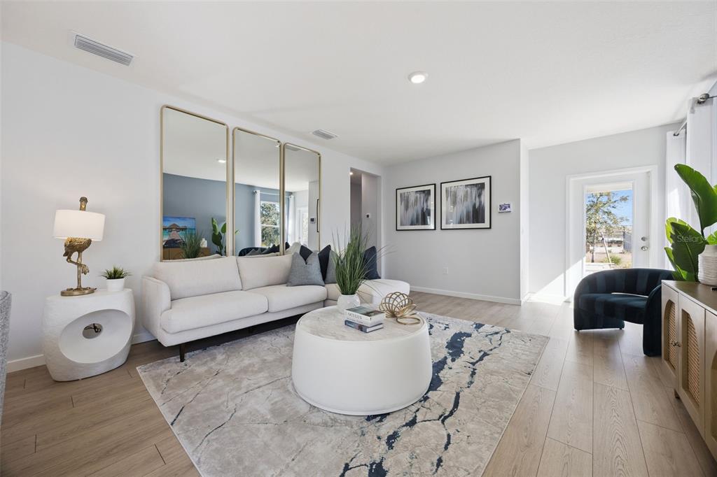 A bright living room features a white sectional sofa, round coffee table, and large wall mirrors — 1358 CAMELLIA BLOOM LANE, SANFORD, FL