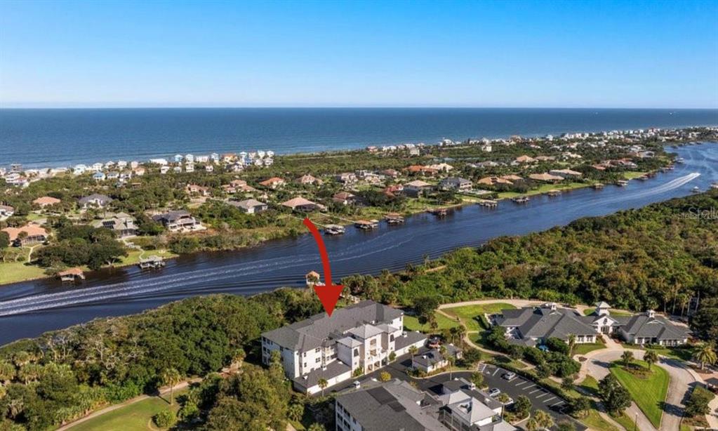An aerial view shows a multi-story residential building near a canal and the ocean — 455 RIVERFRONT DRIVE UNIT A303, PALM COAST, FL