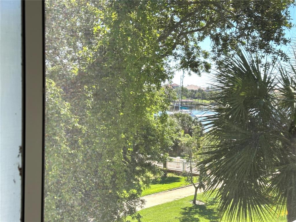 A view of a grassy yard, trees, and a waterway seen through a window screen — 455 RIVERFRONT DRIVE UNIT A303, PALM COAST, FL