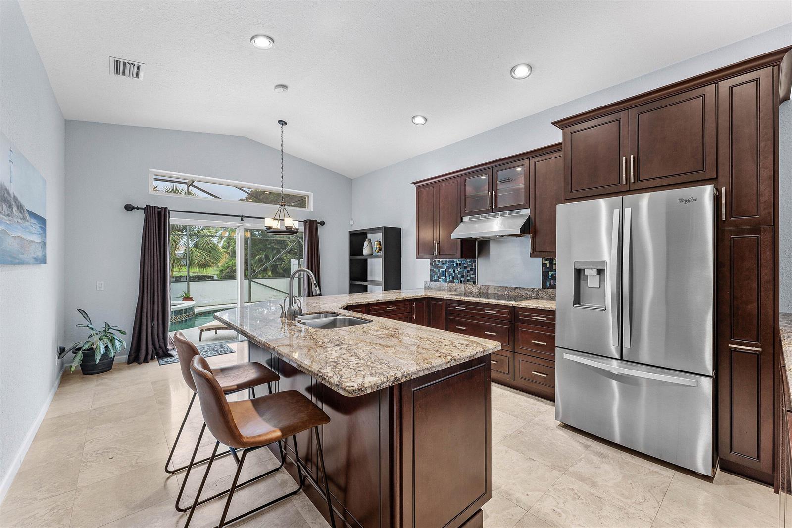 A kitchen with dark wood cabinets, granite countertops, stainless steel appliances, and a pool view — 7076 MIDDLEBURY Drive, Boynton Beach FL 33436, BOYNTON BEACH, FL