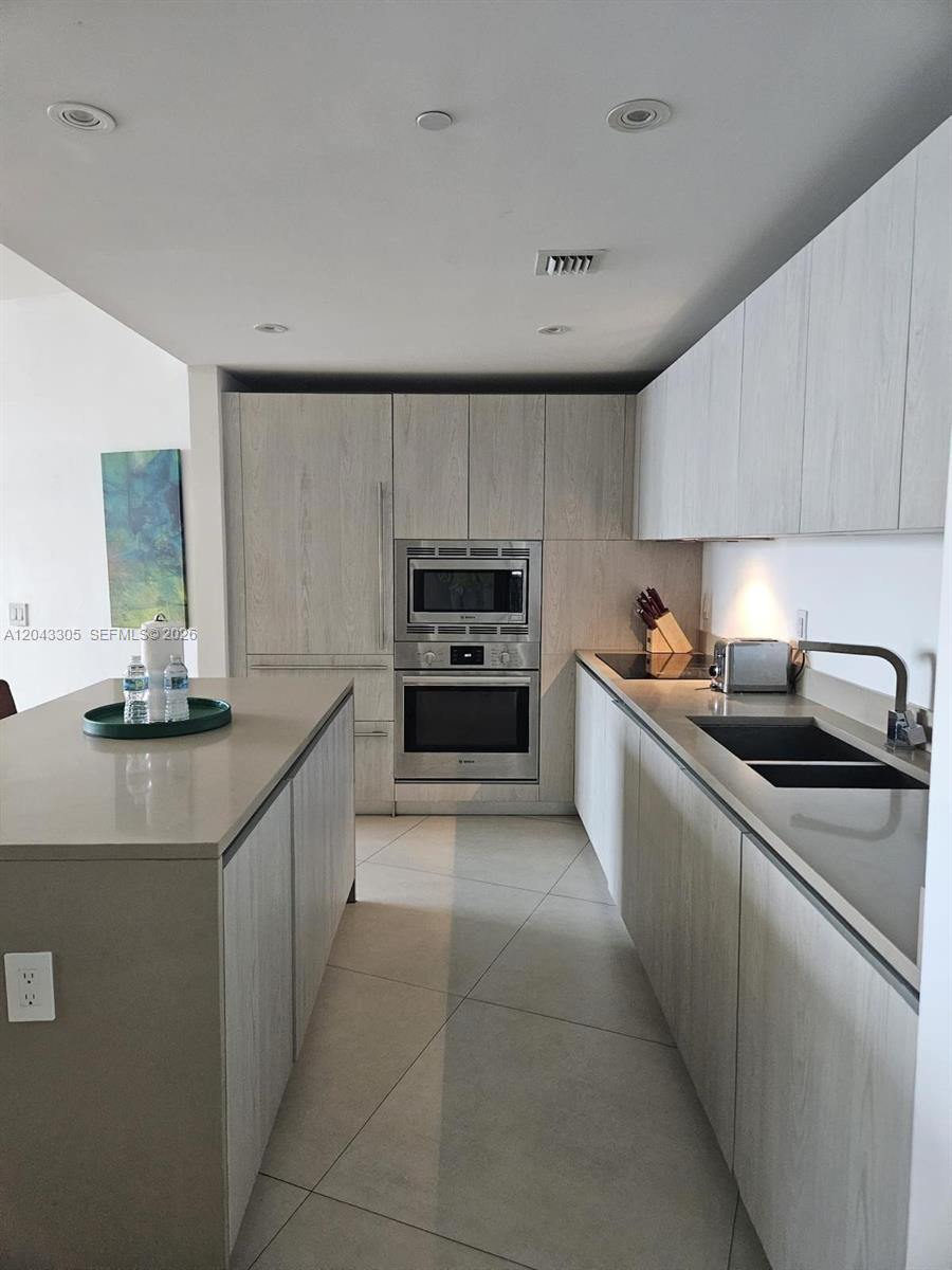 A modern kitchen features light wood cabinetry, a central island, and stainless steel appliances — 4111 S Ocean Dr # 1204, Hollywood FL 33019, HOLLYWOOD, FL