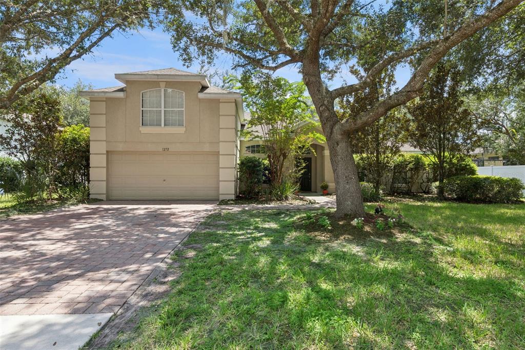 A two-story house with a beige stucco exterior, a two-car garage, and a brick driveway — 1272 BRAMLEY LANE, DELAND, FL