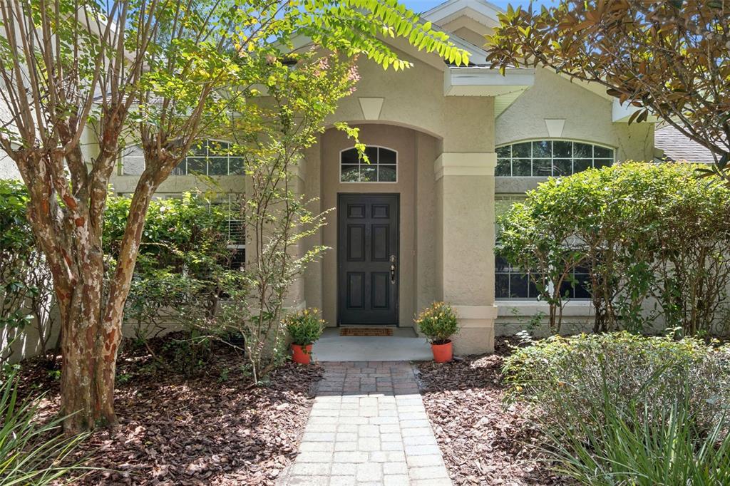 A stone walkway leads to the front entrance of a beige house with a dark door — 1272 BRAMLEY LANE, DELAND, FL