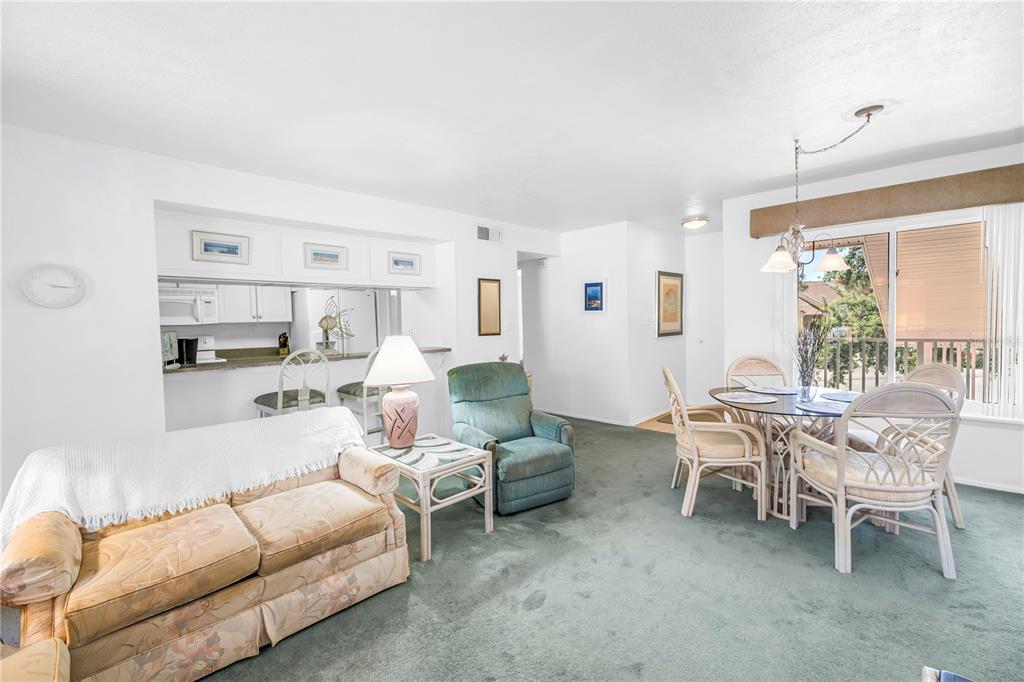 A living and dining area with green carpet, a floral sofa, and a glass-topped table — 3742 41ST WAY S UNIT F, ST PETERSBURG, FL