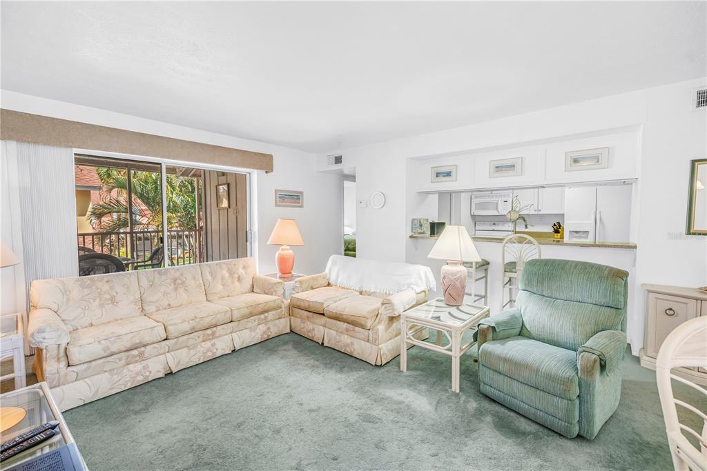 A living room features green carpeting, a floral sofa, a recliner, and an open kitchen — 3742 41ST WAY S UNIT F, ST PETERSBURG, FL