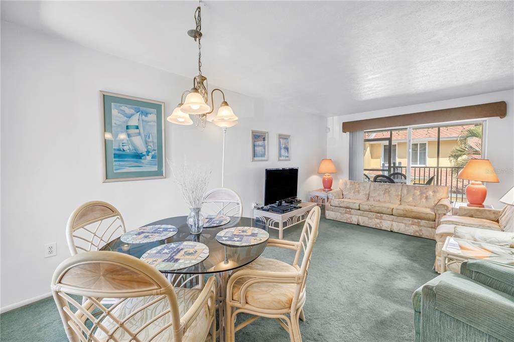 A dining area with a glass table and rattan chairs sits beside a carpeted living room — 3742 41ST WAY S UNIT F, ST PETERSBURG, FL