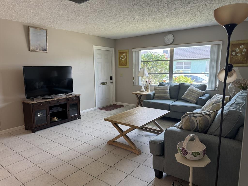 A living room features tile flooring, two gray sofas, a wooden coffee table, and a television — 7007 VERSAILLES N UNIT n/a, PINELLAS PARK, FL