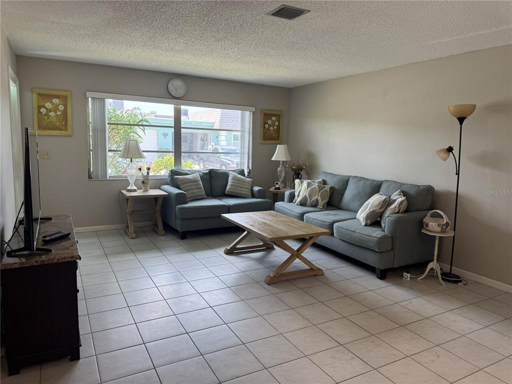 A living room features light tile floors, a blue sofa and loveseat, and a window — 7007 VERSAILLES N UNIT n/a, PINELLAS PARK, FL