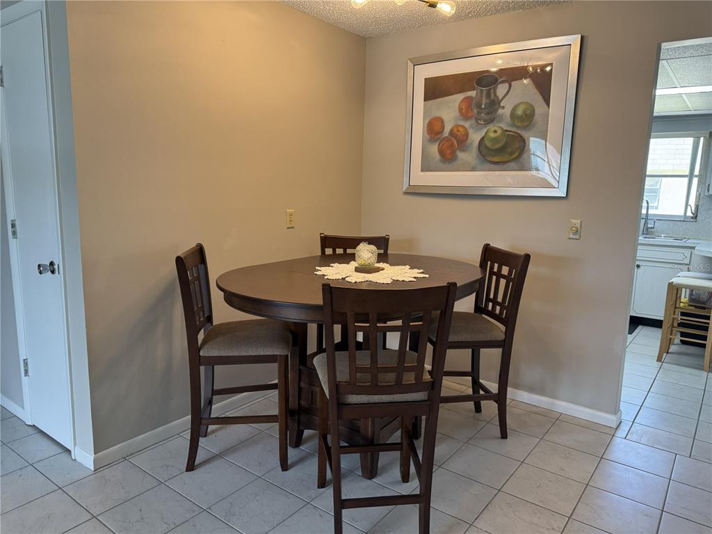 A dining area features a round wooden table with four chairs and a framed painting — 7007 VERSAILLES N UNIT n/a, PINELLAS PARK, FL