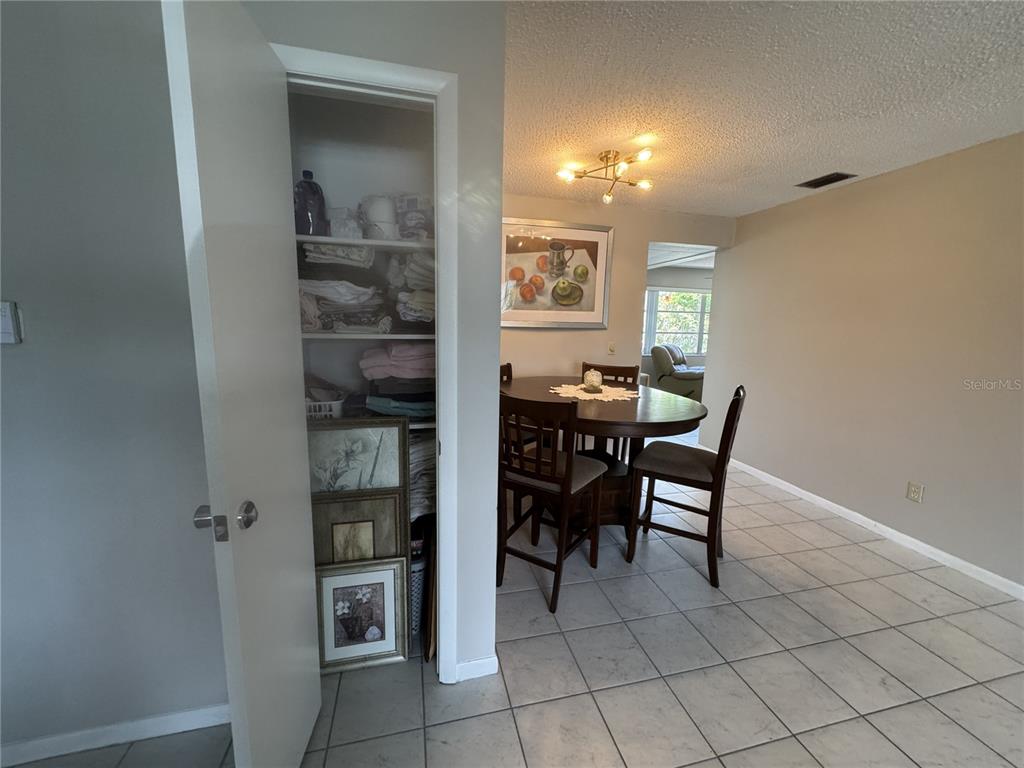 A dining area with a round table and chairs sits next to an open linen closet — 7007 VERSAILLES N UNIT n/a, PINELLAS PARK, FL