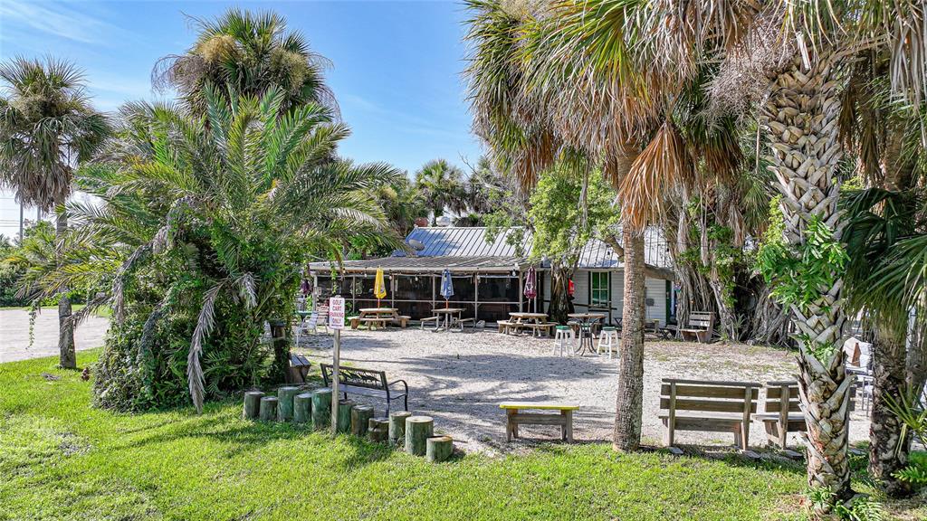An outdoor patio area with picnic tables, benches, and palm trees in front of a building — 4370 GARDEN ROAD, PORT CHARLOTTE, FL