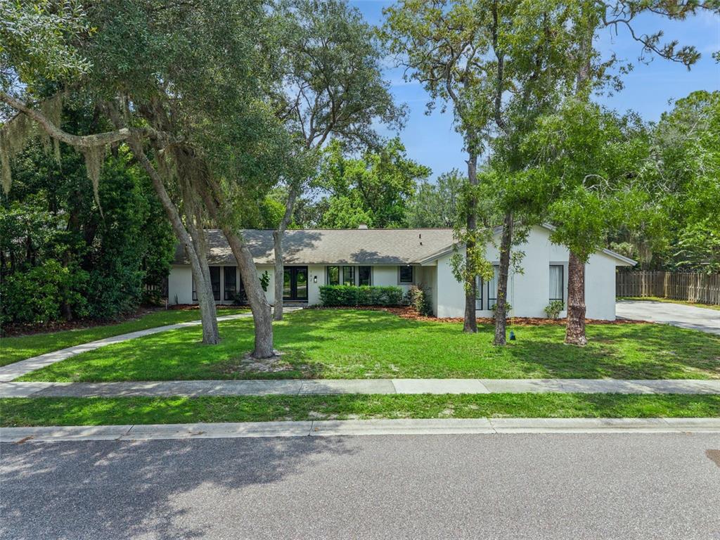 A single-story white house with a gray roof sits behind a lawn and mature trees — 102 STONEBRIDGE DRIVE, LONGWOOD, FL
