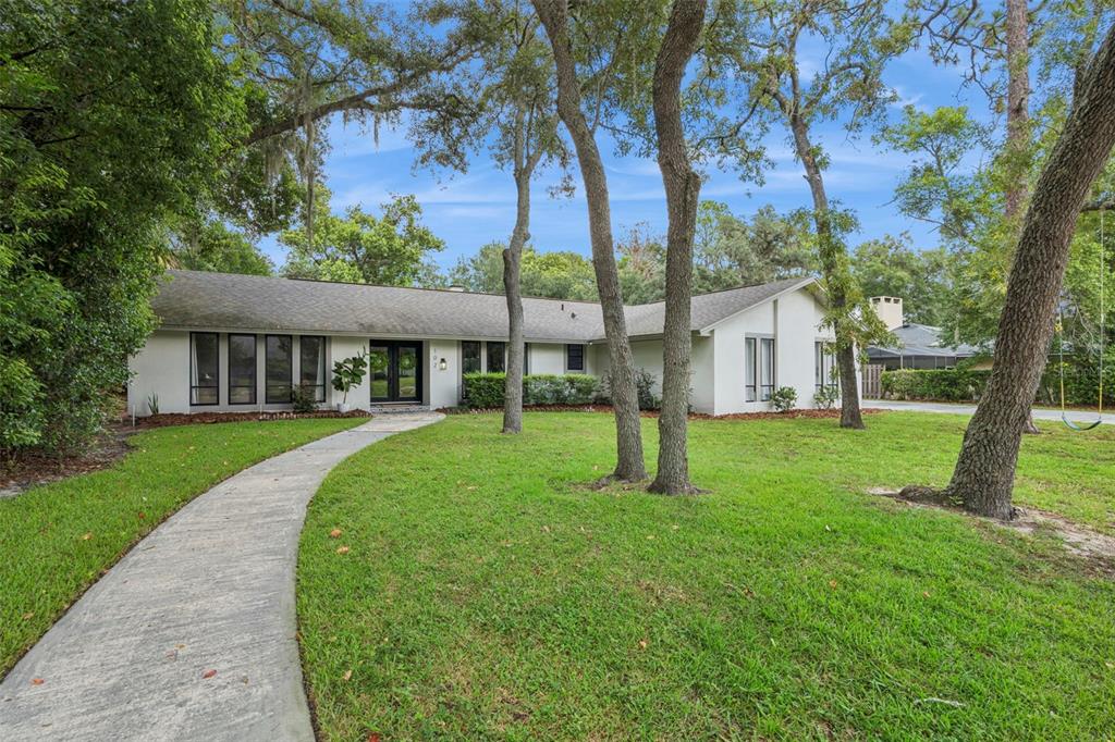 A single-story white house with a curved walkway and mature trees in the front yard — 102 STONEBRIDGE DRIVE, LONGWOOD, FL