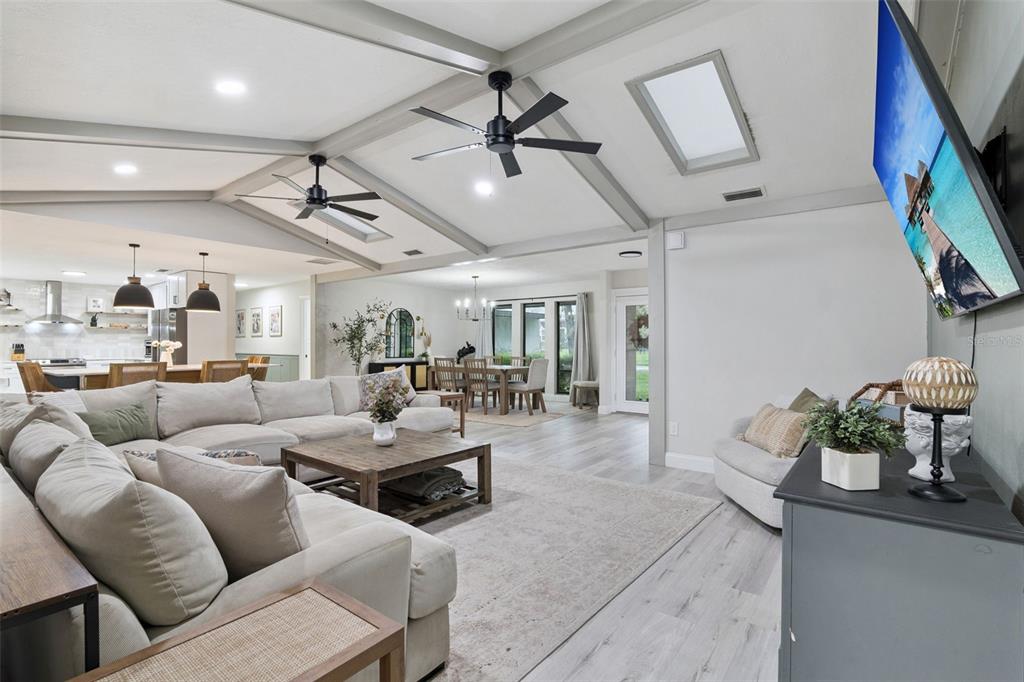 An open-concept living area features a vaulted ceiling with exposed beams, ceiling fans, and skylights — 102 STONEBRIDGE DRIVE, LONGWOOD, FL