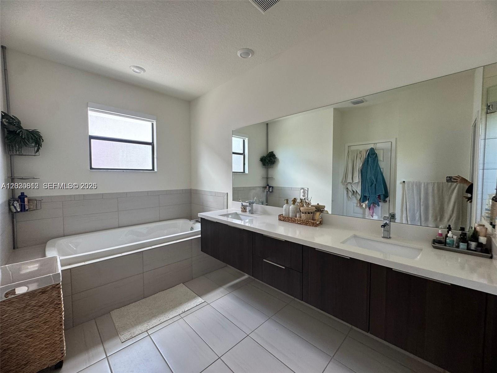 A modern bathroom features a floating double vanity, a soaking tub, and large wall mirror — 10240 NW 76th Ter, Doral FL 33178, DORAL, FL