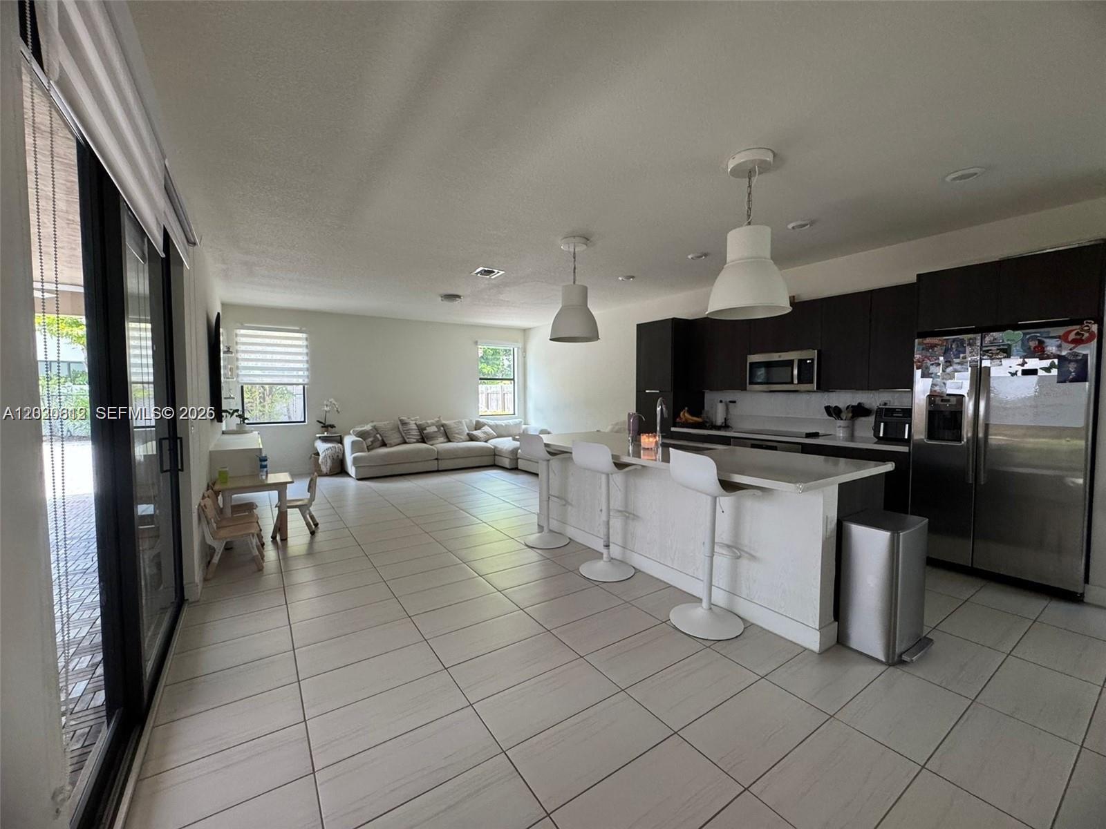 An open-concept kitchen with a white island and bar stools overlooks a living area — 10240 NW 76th Ter, Doral FL 33178, DORAL, FL