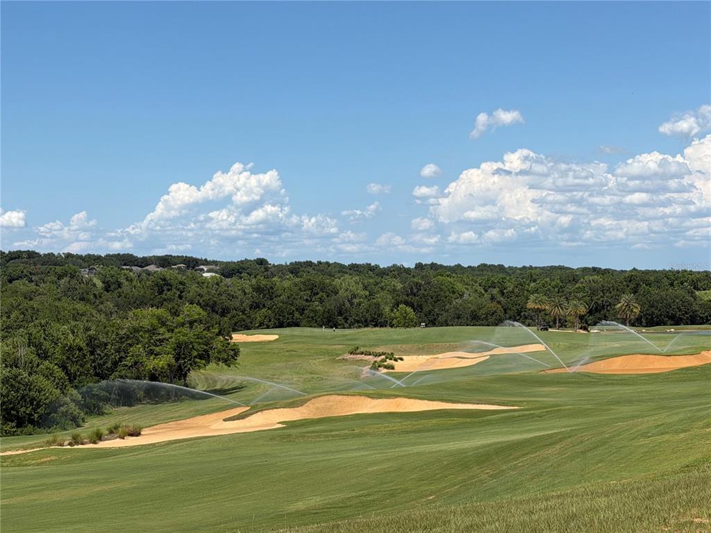 A wide view of a golf course fairway with sand bunkers and active irrigation sprinklers — 15831 VETTA DRIVE, BELLA COLLINA, FL