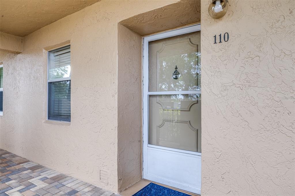 A beige stucco exterior wall features a front door with a screen and number 110 — 90 S HIGHLAND AVENUE UNIT 110, TARPON SPRINGS, FL