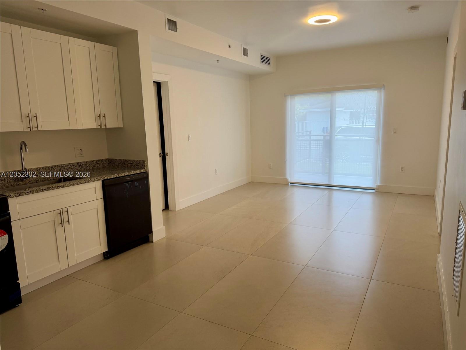 A kitchen with white cabinets and a dishwasher opens into a tiled living area — 2641 NW 24th Ct # 204, Miami FL 33142, MIAMI, FL