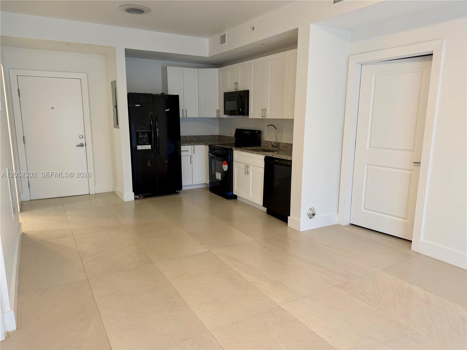 A kitchen with white cabinets, black appliances, and light tile flooring in an open space — 2641 NW 24th Ct # 204, Miami FL 33142, MIAMI, FL
