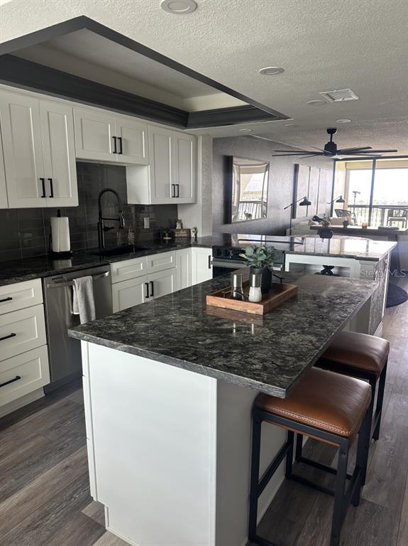 A kitchen features white cabinets, dark granite countertops, a center island, and two bar stools — 9425 BLIND PASS ROAD UNIT 1207, ST PETERSBURG, FL