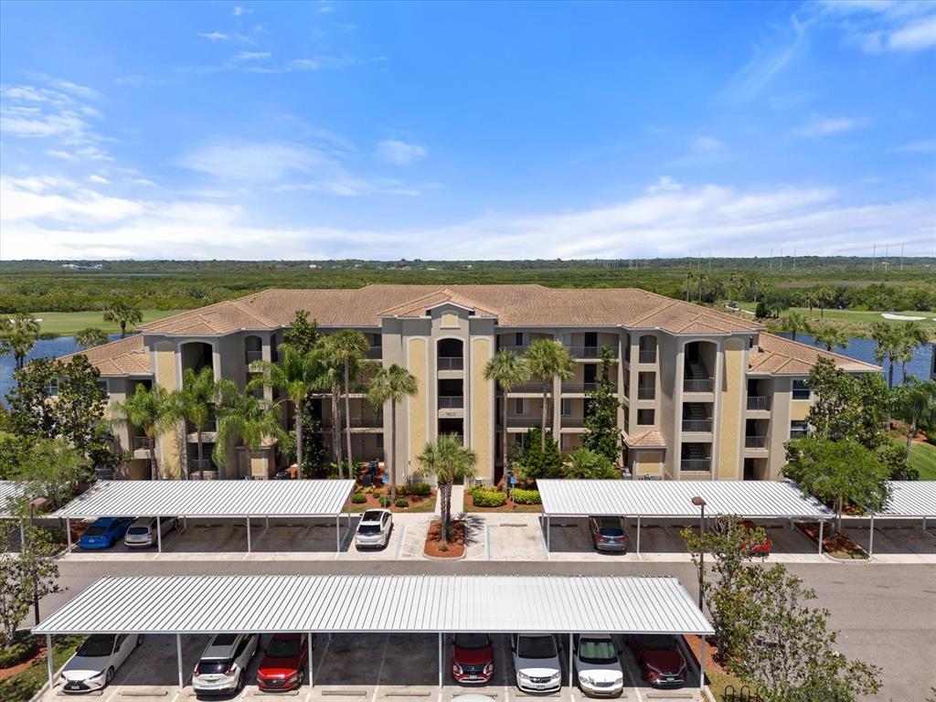 An aerial view of a multi-story apartment building with covered parking spaces in the foreground — 7803 GRAND ESTUARY TRAIL UNIT 308, BRADENTON, FL