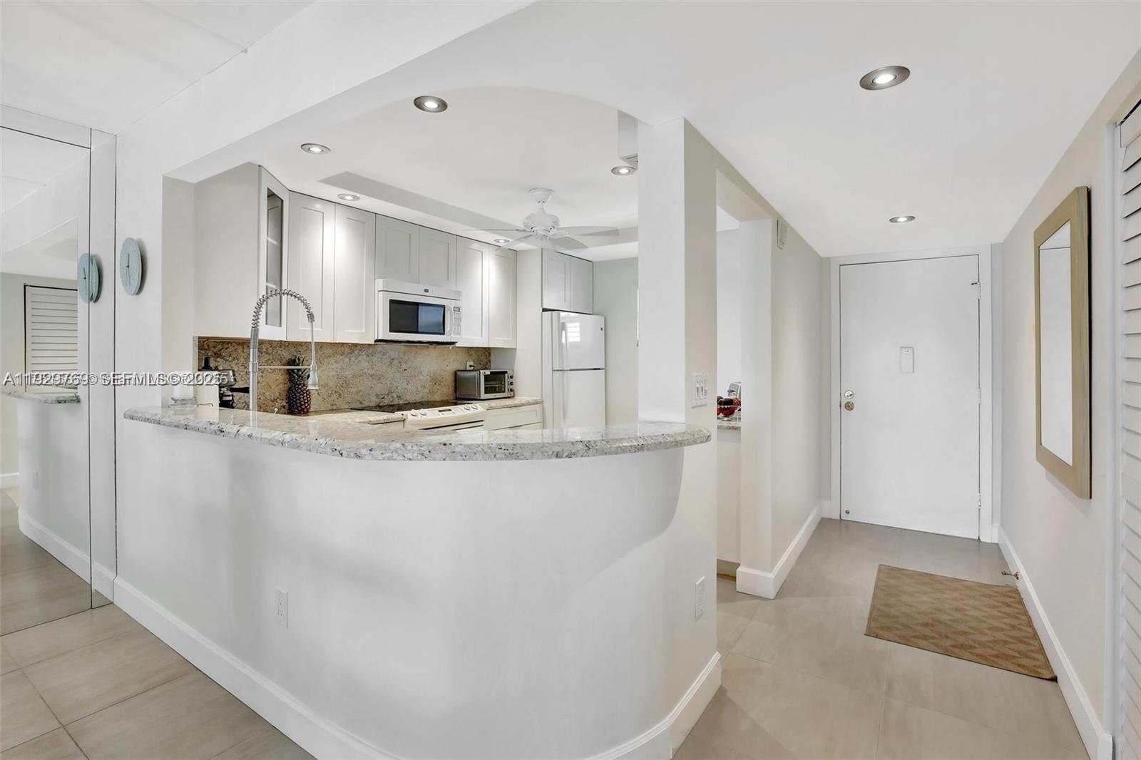 A kitchen with white cabinets and granite countertops overlooks a tiled entryway with a door — 3930 Inverrary Blvd # D, Lauderhill FL 33319, LAUDERHILL, FL