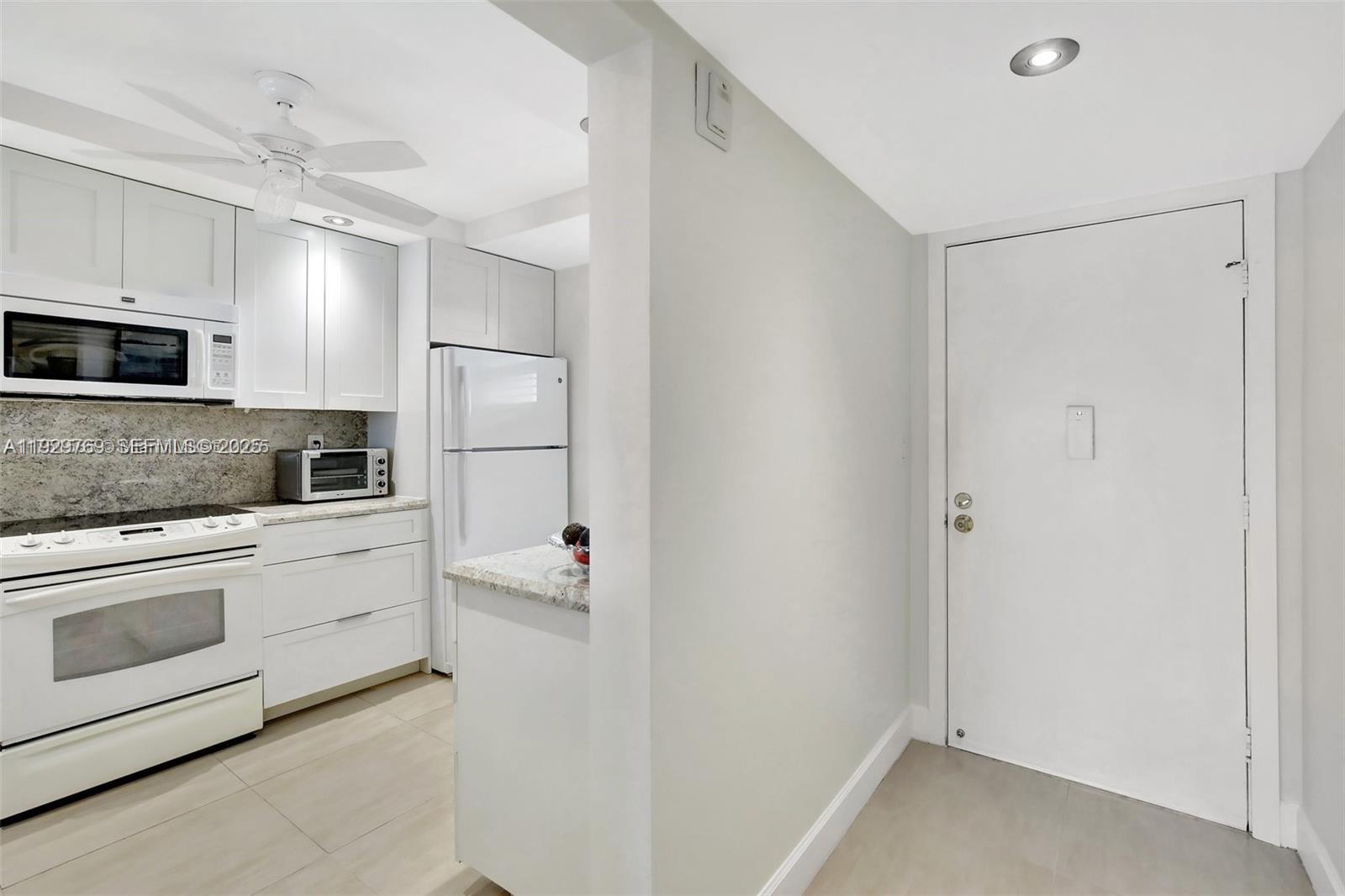 A white kitchen features granite countertops, stainless steel appliances, and an adjacent entryway door — 3930 Inverrary Blvd # D, Lauderhill FL 33319, LAUDERHILL, FL