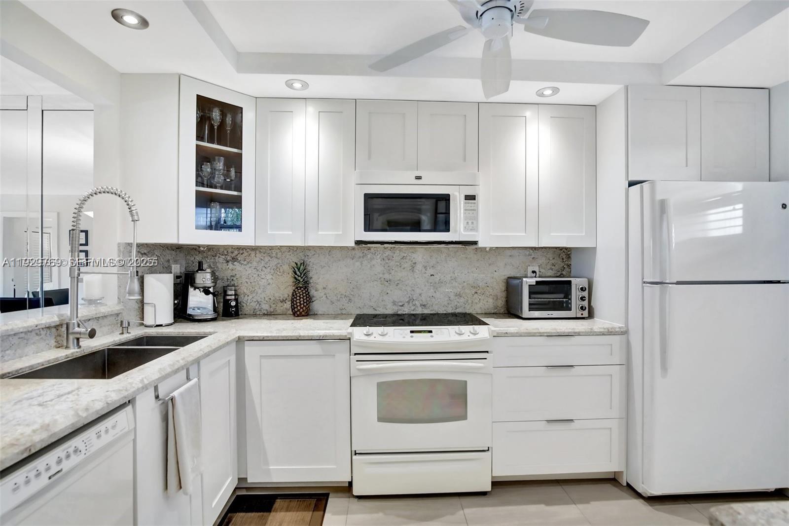 A white kitchen features granite countertops, stainless steel appliances, and a glass-front upper cabinet — 3930 Inverrary Blvd # D, Lauderhill FL 33319, LAUDERHILL, FL