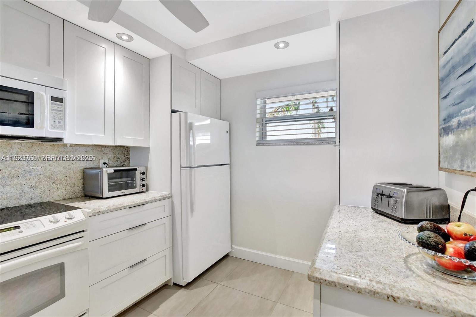 A white kitchen features granite countertops, stainless steel appliances, and light-colored cabinetry — 3930 Inverrary Blvd # D, Lauderhill FL 33319, LAUDERHILL, FL