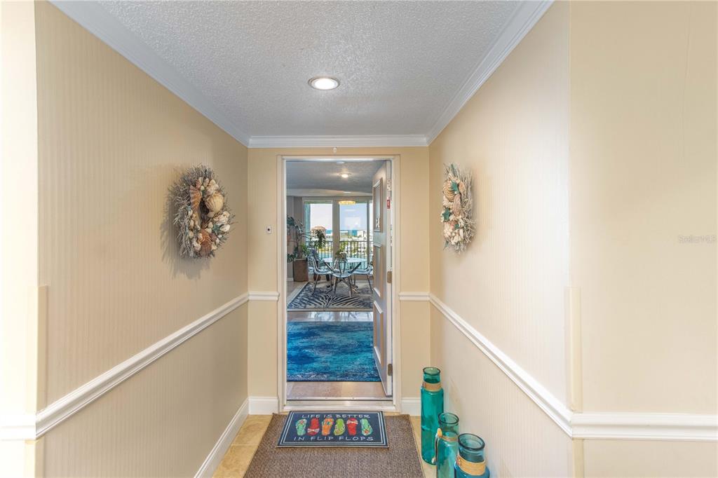 A hallway with beige walls, chair rail molding, and a doorway leading to a balcony — 736 ISLAND WAY UNIT 804, CLEARWATER, FL