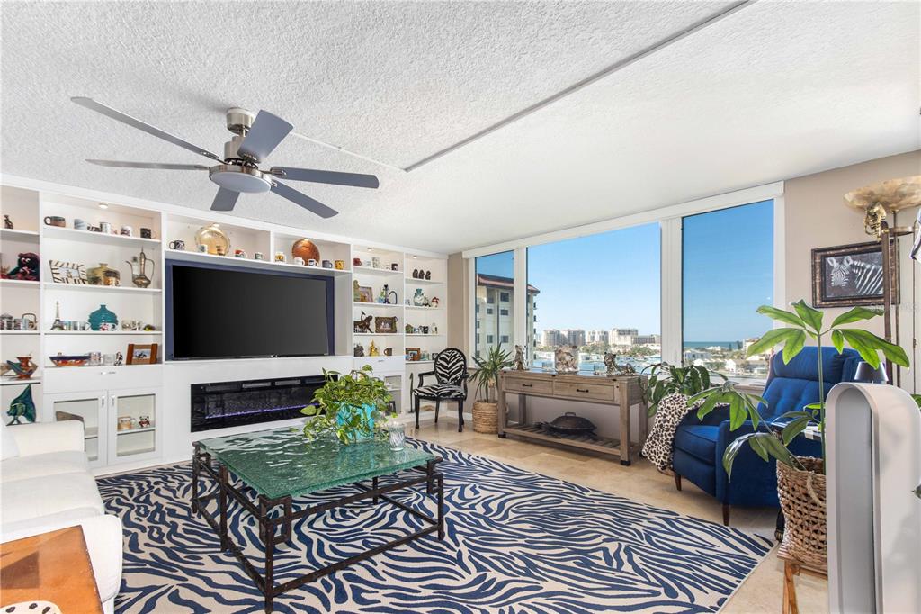 A living room features a zebra-print rug, built-in shelving, a fireplace, and floor-to-ceiling windows — 736 ISLAND WAY UNIT 804, CLEARWATER, FL
