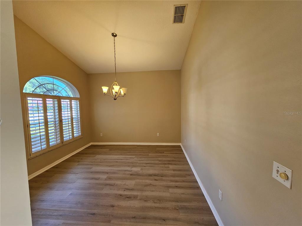 An empty dining room features wood-look flooring, a chandelier, and a large arched window — 17817 SE 115TH COURT, SUMMERFIELD, FL