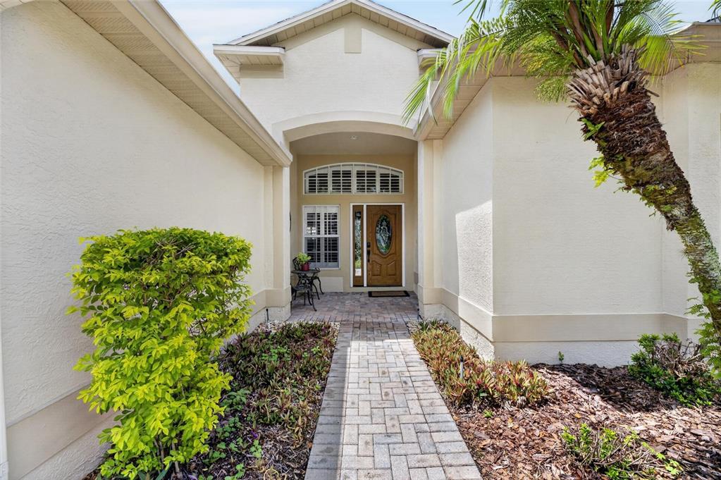 A paved walkway leads to the front entrance of a house with a palm tree — 18116 KARA CT, TAMPA, FL