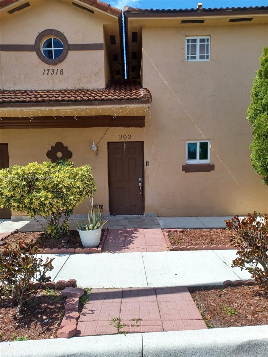 The exterior of a two-story stucco townhouse features a brown front door and a circular window — 17316 NW 74th Ave # 202, Hialeah FL 33015, HIALEAH, FL
