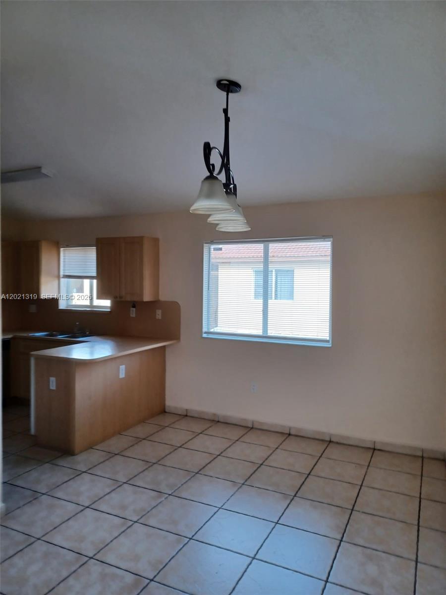 A kitchen with light wood cabinets and tile flooring features a dining area with a chandelier — 17316 NW 74th Ave # 202, Hialeah FL 33015, HIALEAH, FL
