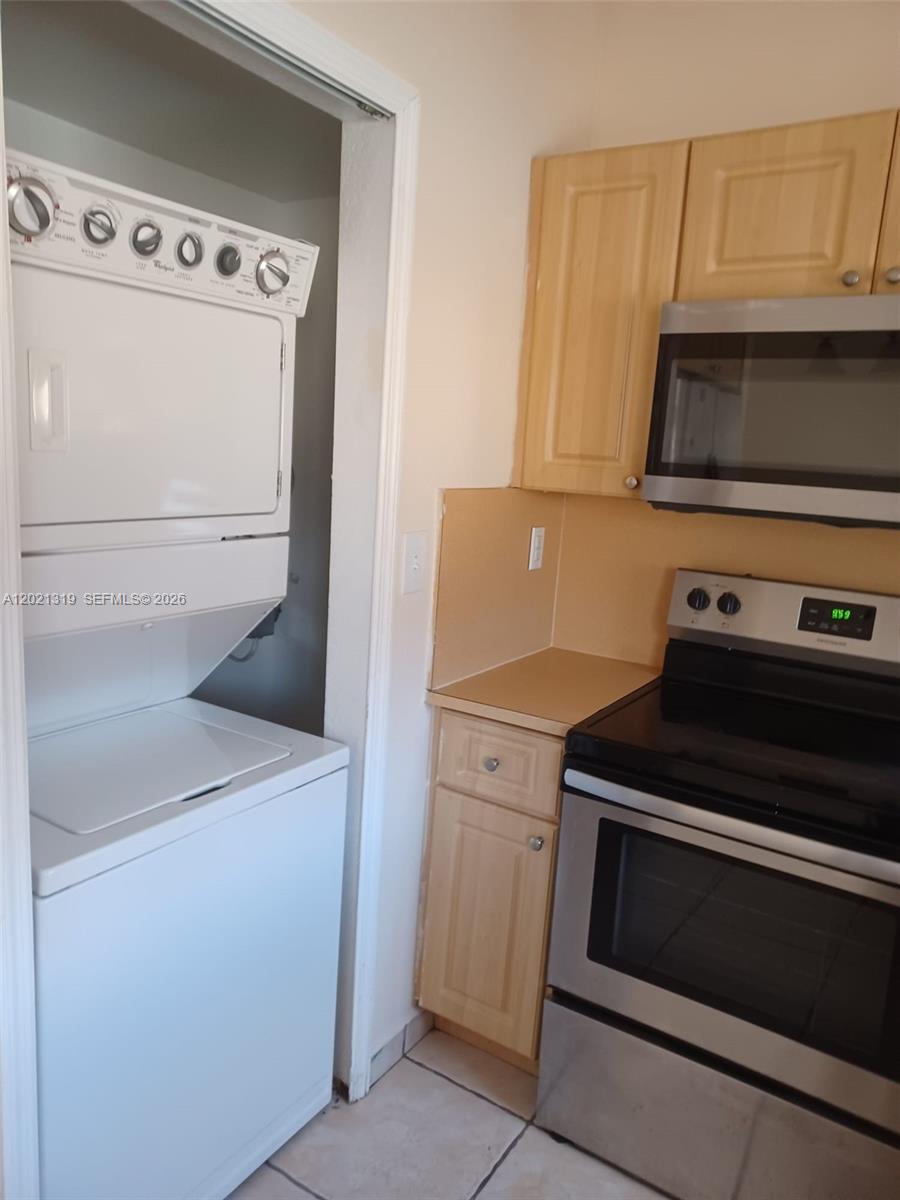A kitchen features a stacked washer and dryer unit next to a stainless steel stove — 17316 NW 74th Ave # 202, Hialeah FL 33015, HIALEAH, FL