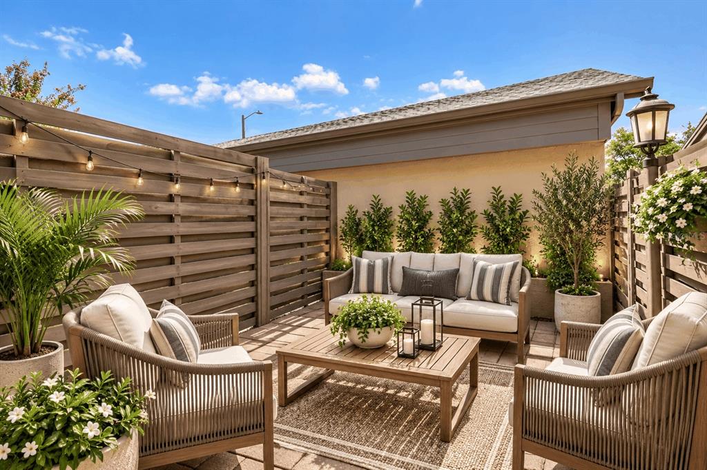 A furnished outdoor patio features a wooden sofa, two armchairs, a coffee table, and string lights — 3157 LANDMARK DRIVE UNIT 414, CLEARWATER, FL