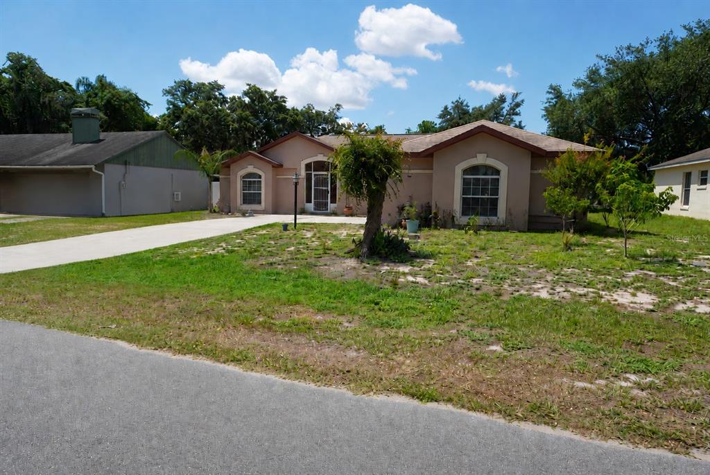 A single-story tan house with a concrete driveway and a sparse, grassy front yard — 11130 FOUNTAIN LAKE BOULEVARD, LEESBURG, FL