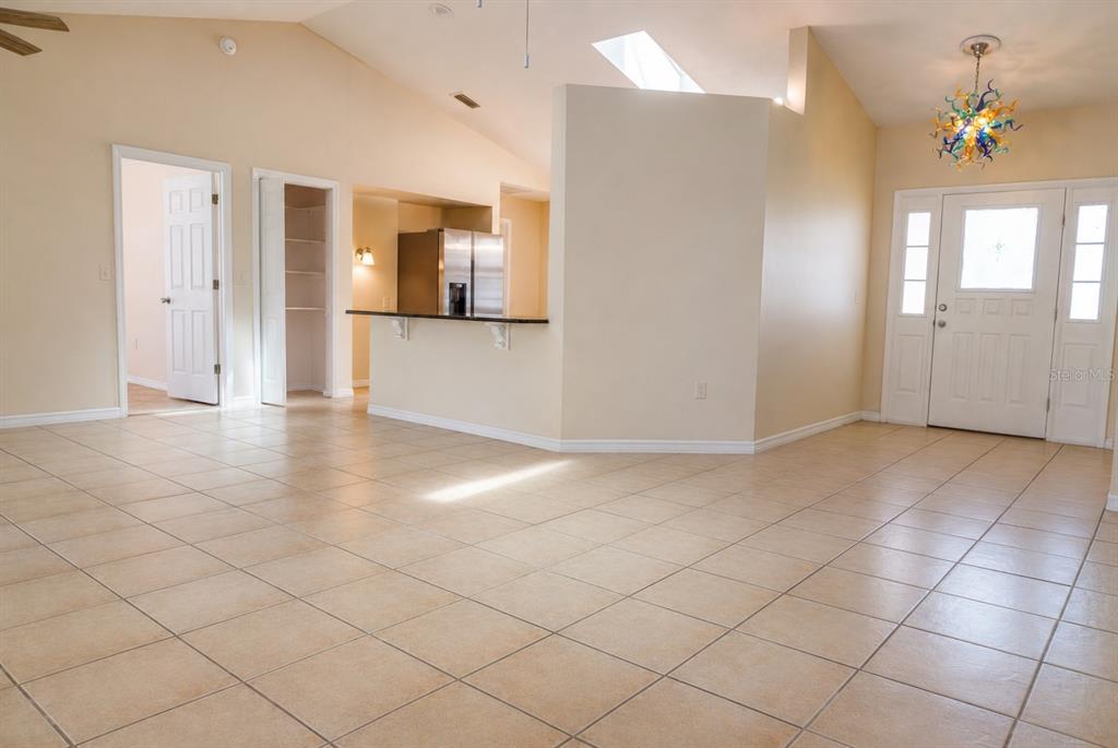 A bright, open-concept living area features beige tile flooring, a kitchen breakfast bar, and vaulted ceilings — 11130 FOUNTAIN LAKE BOULEVARD, LEESBURG, FL