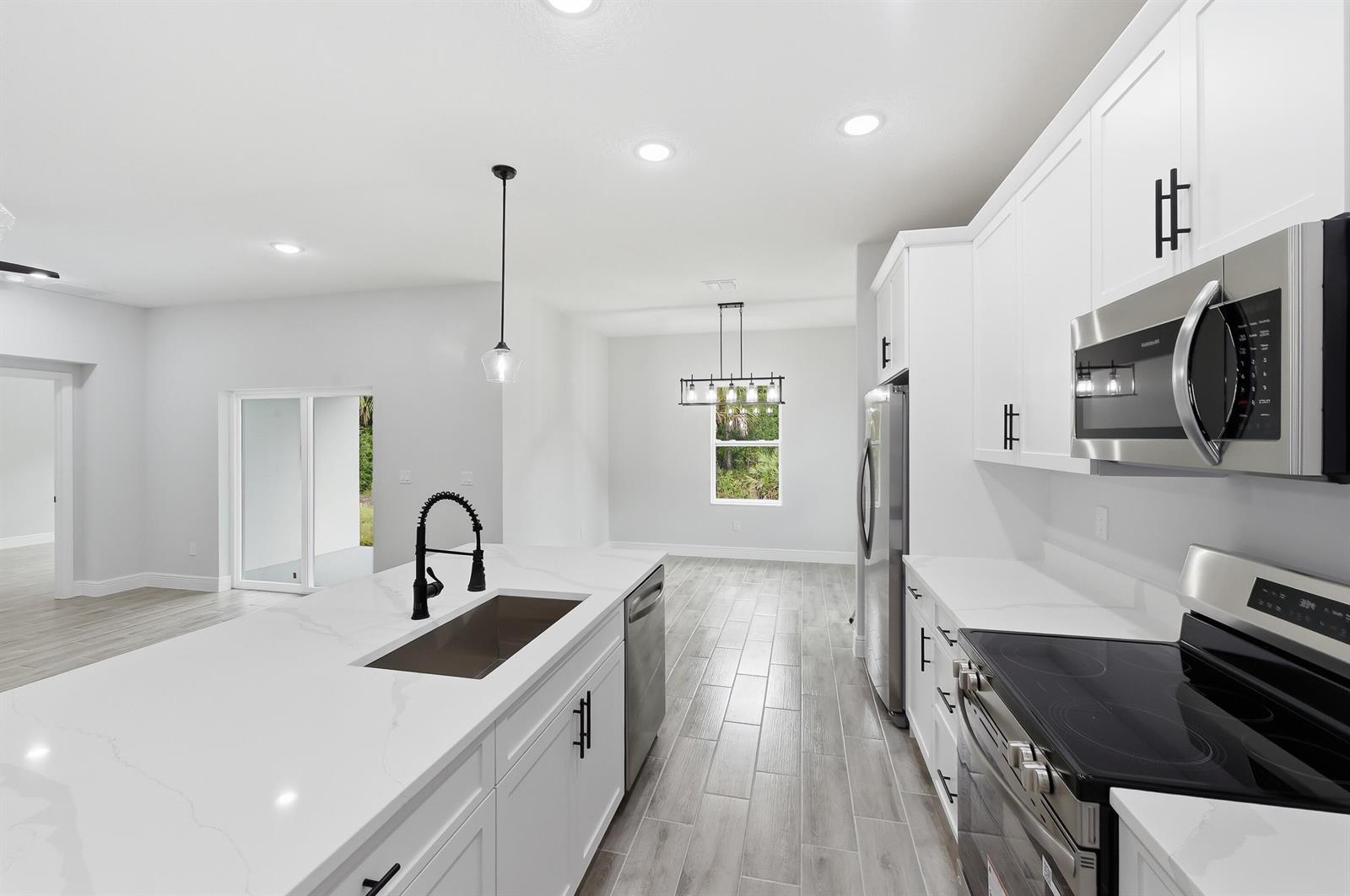 A modern kitchen features white cabinets, quartz countertops, stainless steel appliances, and gray wood-look flooring — 7825 96th Avenue, Vero Beach FL 32967, VERO BEACH, FL