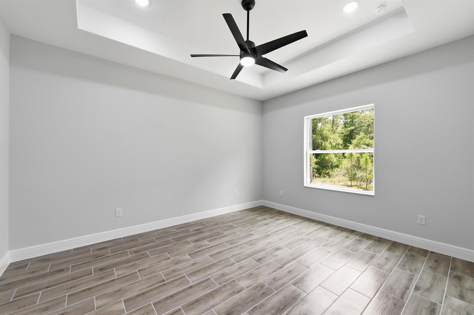 An empty bedroom features light gray walls, wood-look tile flooring, and a tray ceiling — 7825 96th Avenue, Vero Beach FL 32967, VERO BEACH, FL