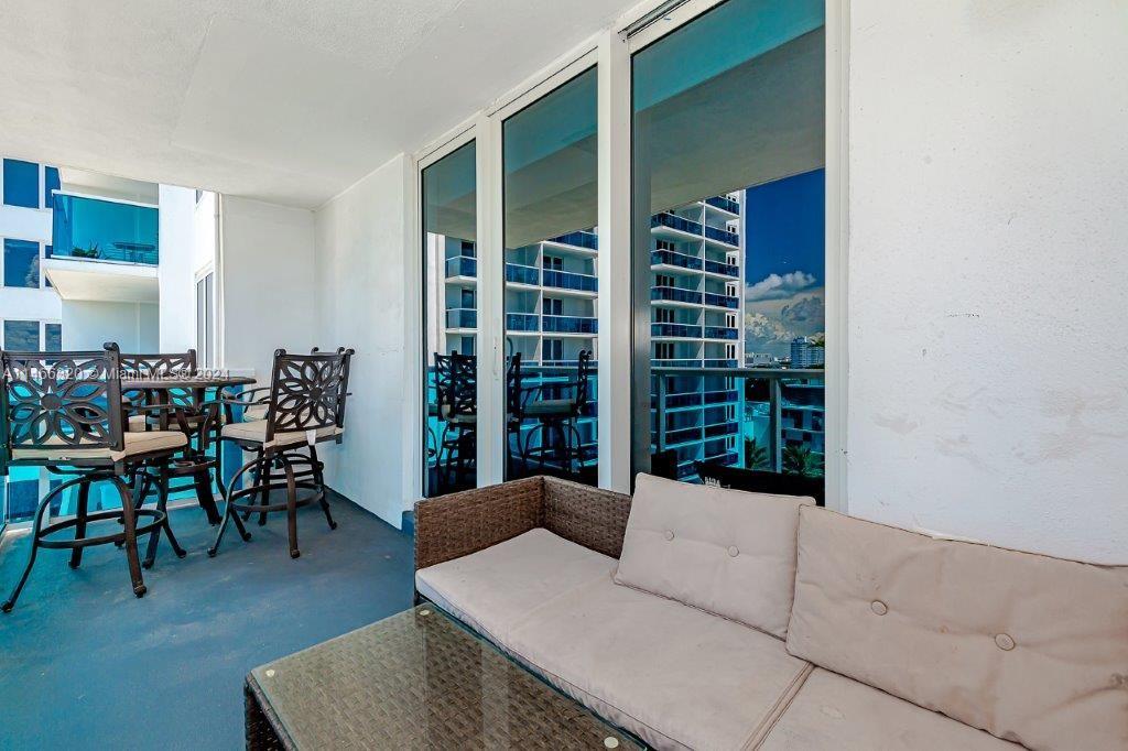 A balcony features a wicker sofa, a glass-topped table, and outdoor chairs overlooking another building — 2301 Collins Ave # 803, Miami Beach FL 33139, MIAMI BEACH, FL