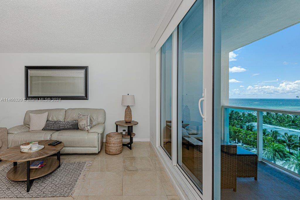 A living room features a white sofa, a coffee table, and sliding doors overlooking the ocean — 2301 Collins Ave # 803, Miami Beach FL 33139, MIAMI BEACH, FL