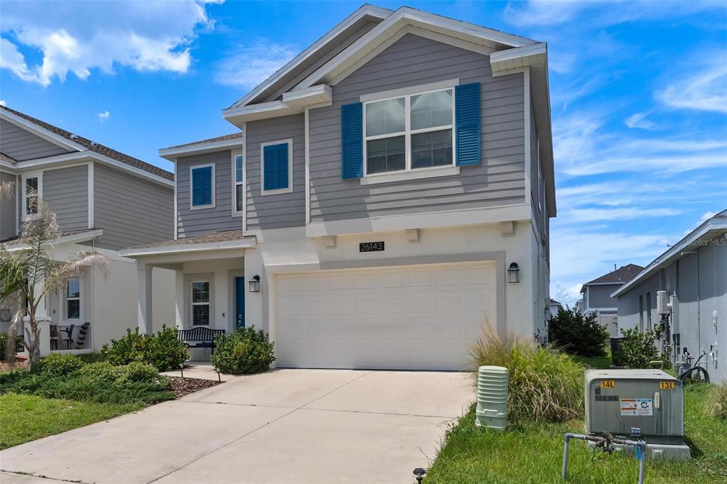 A two-story suburban house with gray siding, blue shutters, and a white two-car garage — 26143 FEATHERGRASS CIRCLE, LEESBURG, FL