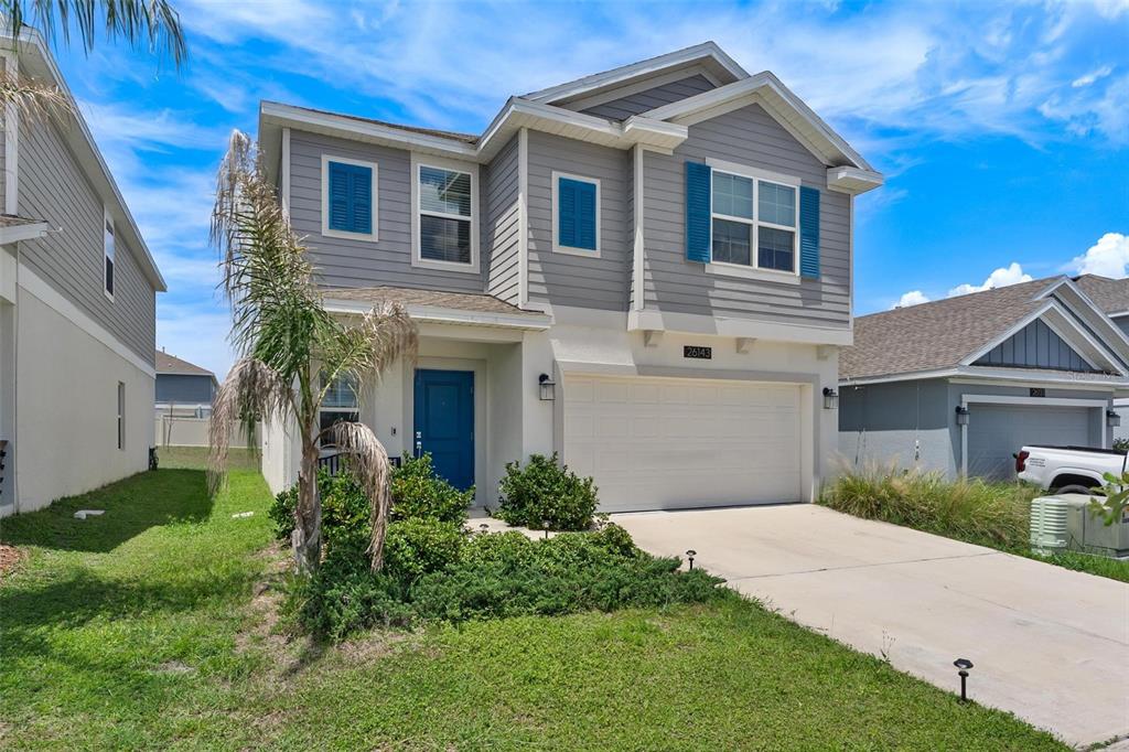 A two-story suburban house features gray siding, a blue front door, and a concrete driveway — 26143 FEATHERGRASS CIRCLE, LEESBURG, FL