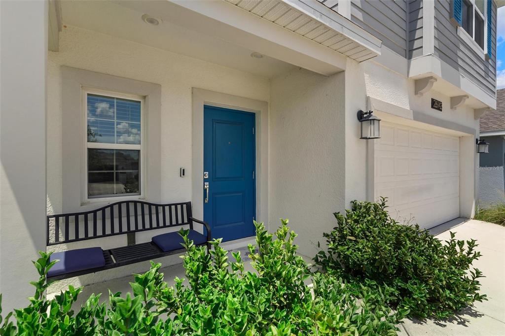 A blue front door is centered on a covered porch with a black metal bench — 26143 FEATHERGRASS CIRCLE, LEESBURG, FL
