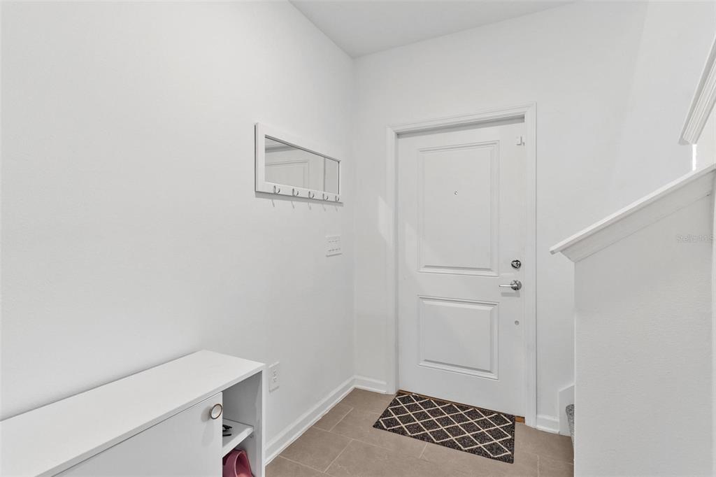 A bright entryway features a white door, a coat rack with a mirror, and tile flooring — 26143 FEATHERGRASS CIRCLE, LEESBURG, FL